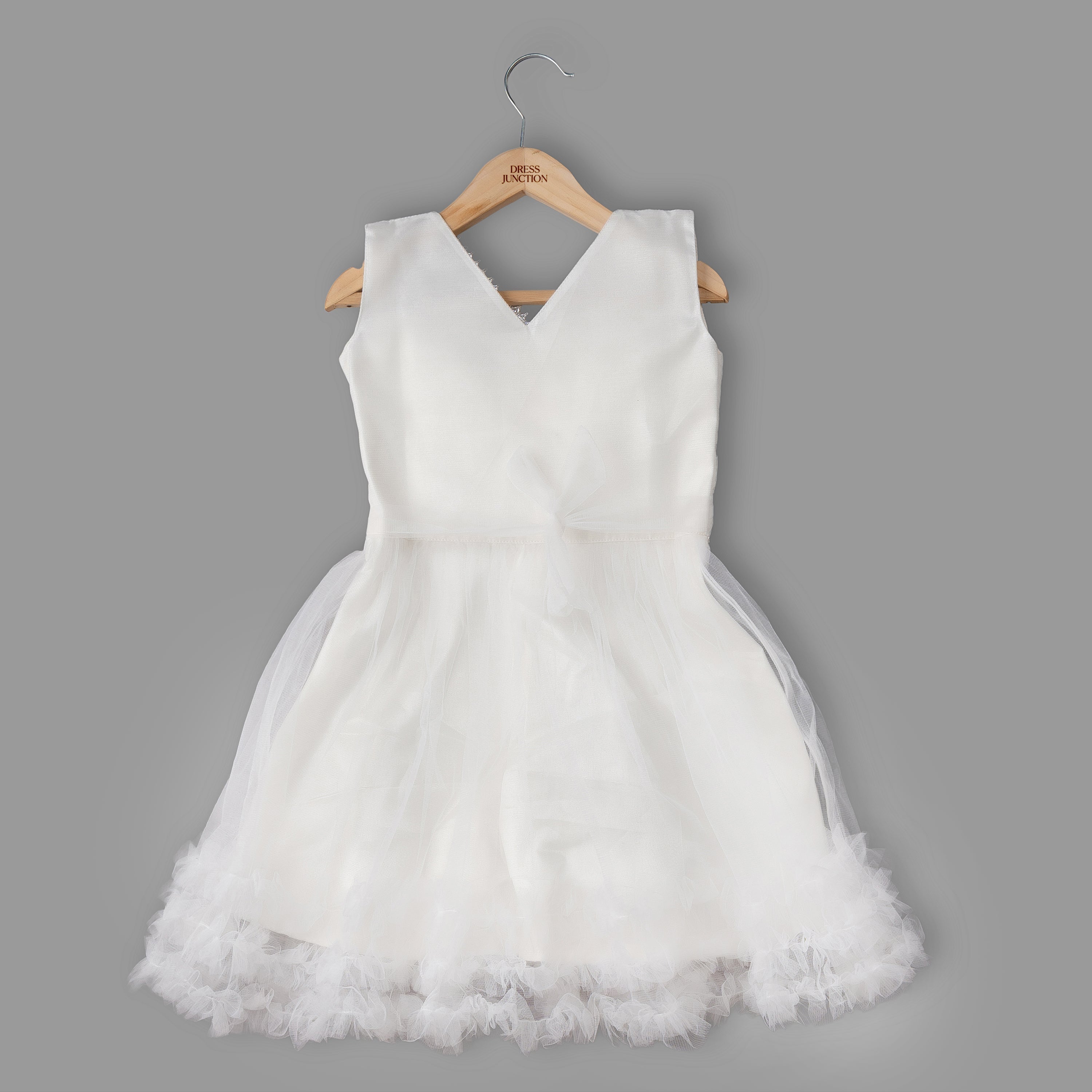 White dress with a tulle skirt on a wooden hanger against a gray background
