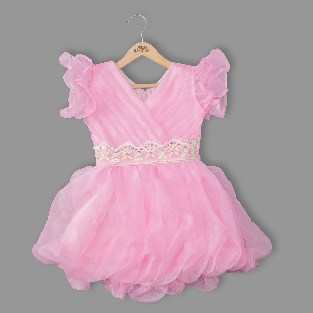Pink dress with ruffled sleeves on a hanger against a gray background