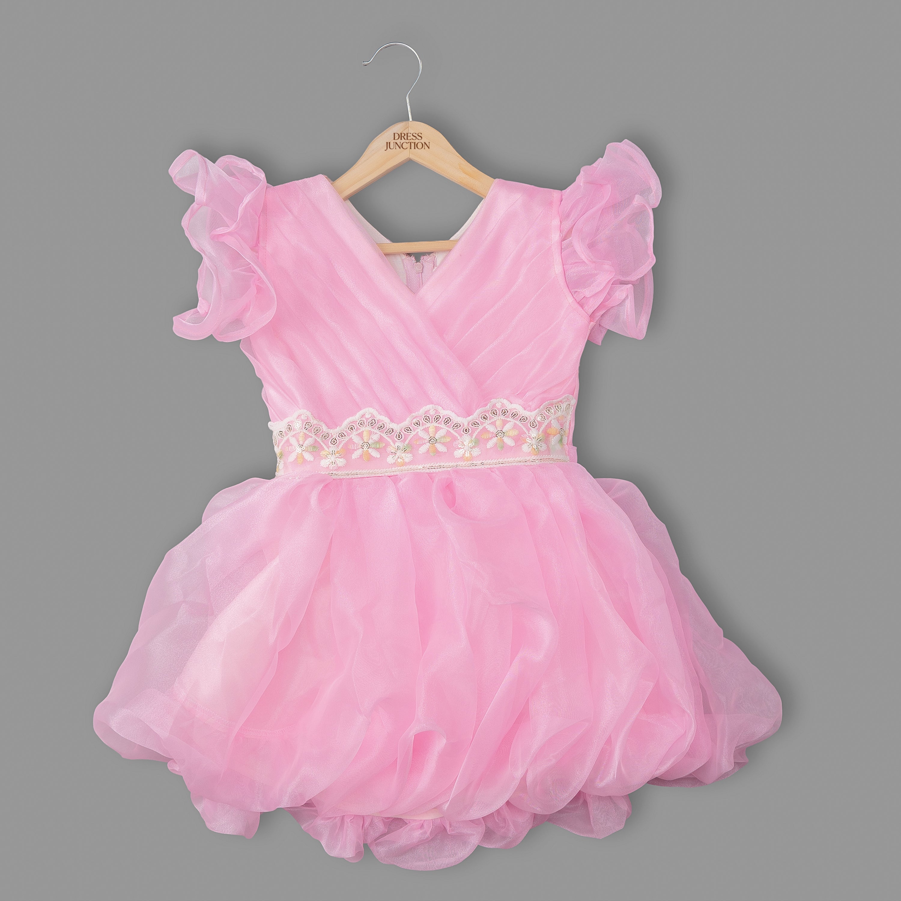 Pink dress with ruffled sleeves on a hanger against a gray background