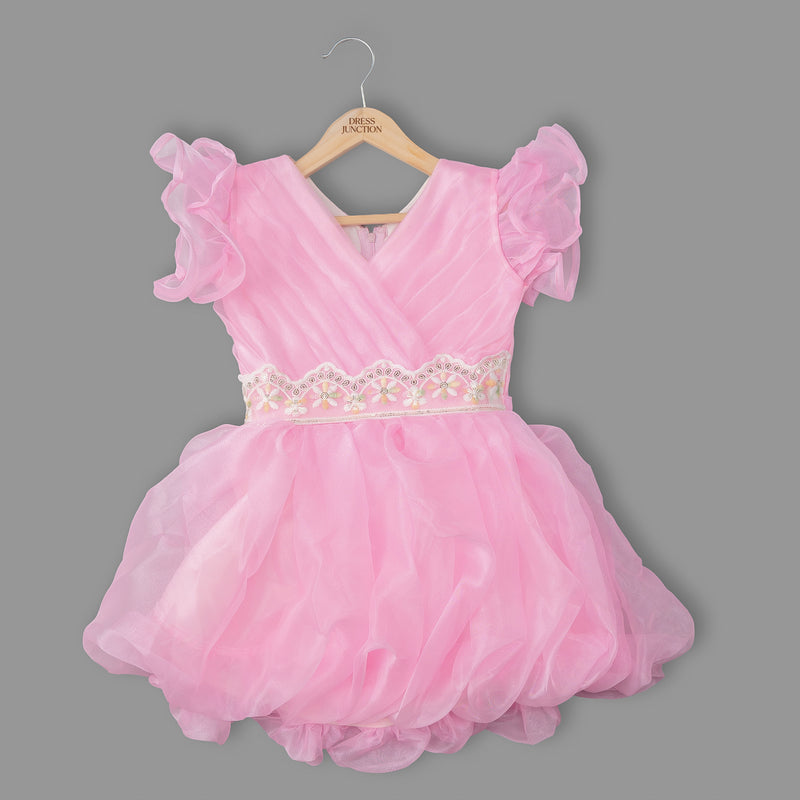 Pink dress with ruffled sleeves on a hanger against a gray background