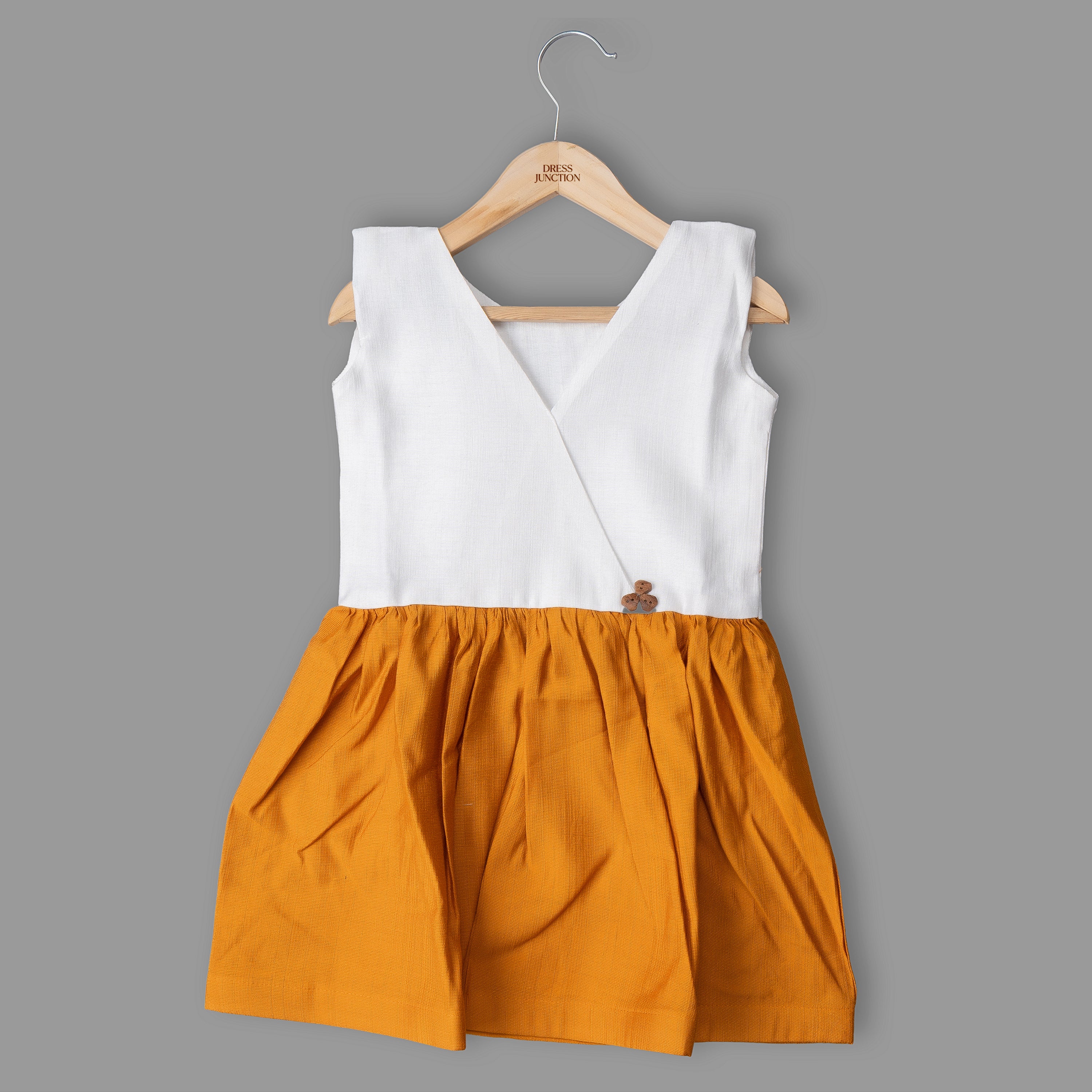 White top and orange skirt dress on a wooden hanger against a gray background